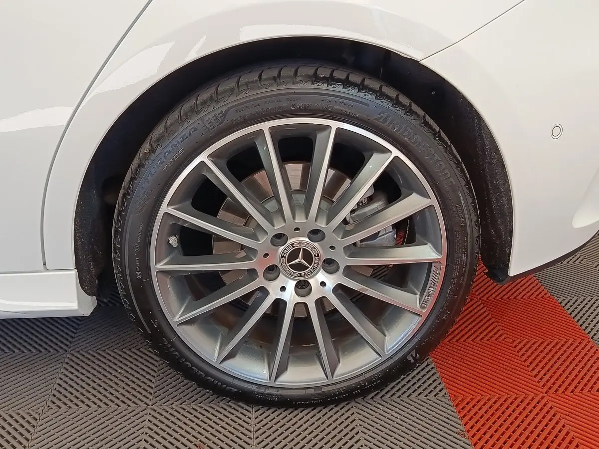 Gros plan sur la roue avant droite avec jante alliage gris et logo Mercedes sur une Mercedes Classe A blanche.