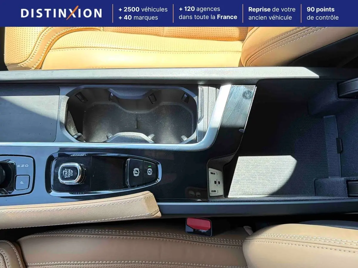 Vue rapprochée de la console centrale beige du Volvo XC90 T8 hybride avec bouton start/stop et porte-gobelets.