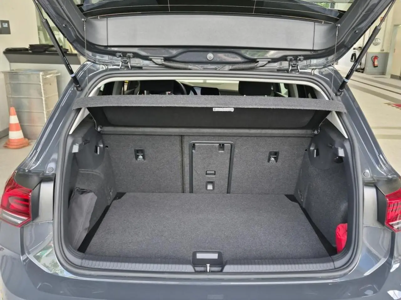 Coffre ouvert vu de l'arrière d'une Volkswagen Golf 8 gris Urano, montrant l'espace de chargement et la plage arrière.