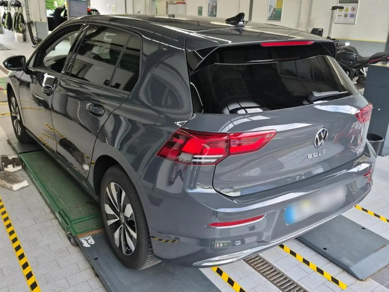 Vue 3/4 arrière droite d'une Volkswagen Golf 8 gris Urano avec feux arrière LED et jantes alliage Norfolk.