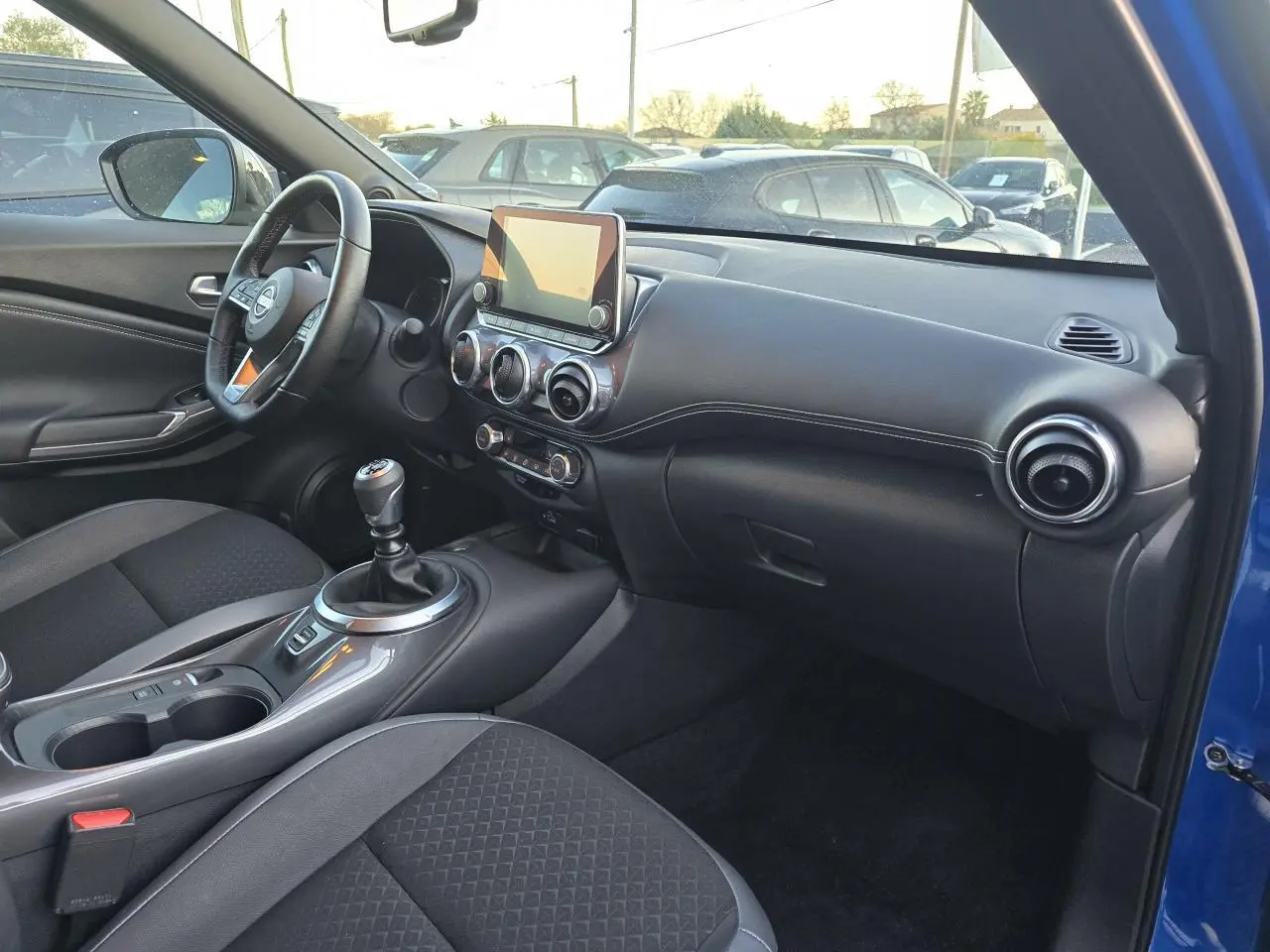 Intérieur côté passager du Nissan Juke II bleu magnetic 2024, avec tableau de bord noir et console centrale moderne.