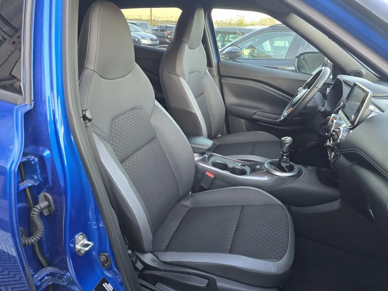 Intérieur avant droit du Nissan Juke II bleu magnetic 2024, sièges TEP/tissu noirs et console centrale avec boîte manuelle.