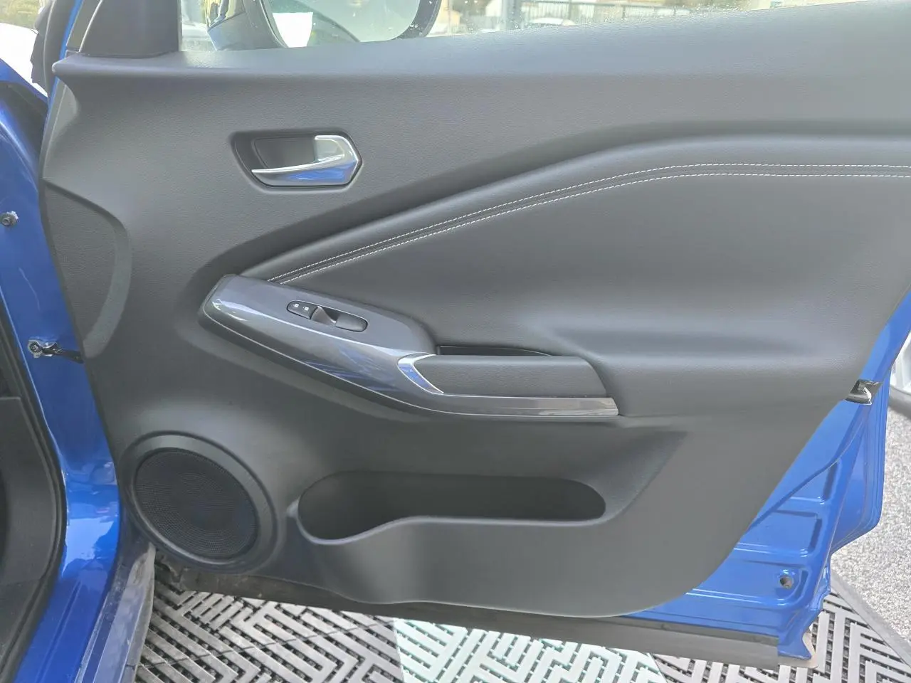 Détail de la porte avant gauche bleu magnetic du Nissan Juke II avec commande de lève-vitre et haut-parleur intégré.