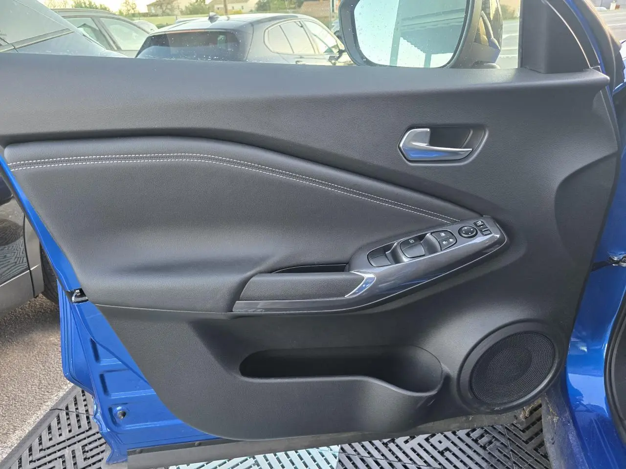 Vue côté gauche de la porte avant bleu magnetic du Nissan Juke II avec commandes de vitres et haut-parleur intégré.