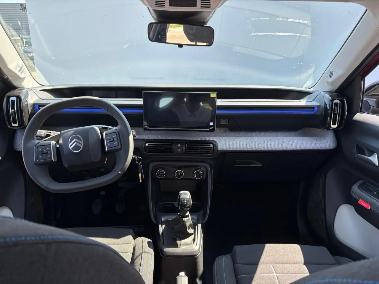 Vue intérieure avant de la Citroën C3 2025 rouge Elixir, tableau de bord avec écran tactile et volant multifonctions noir.