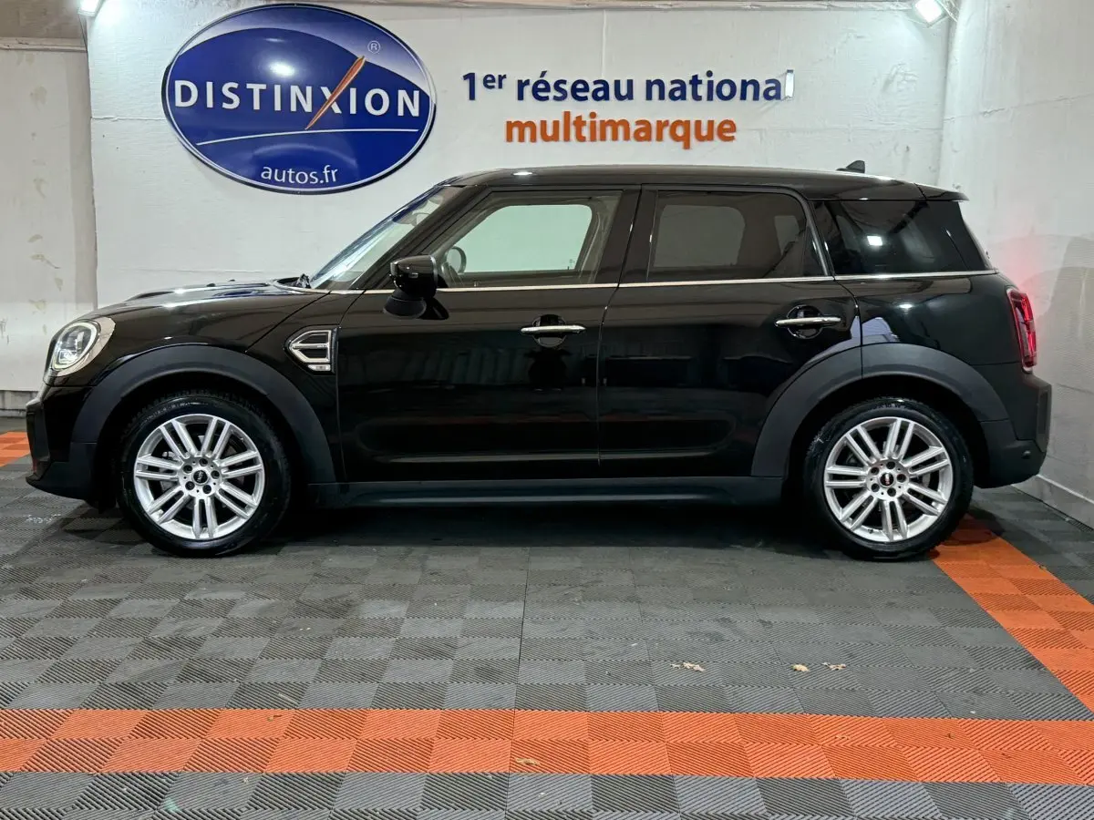 Profil côté gauche d'une MINI COUNTRYMAN Cooper D Business Design noire, vue en intérieur sur sol gris et orange.