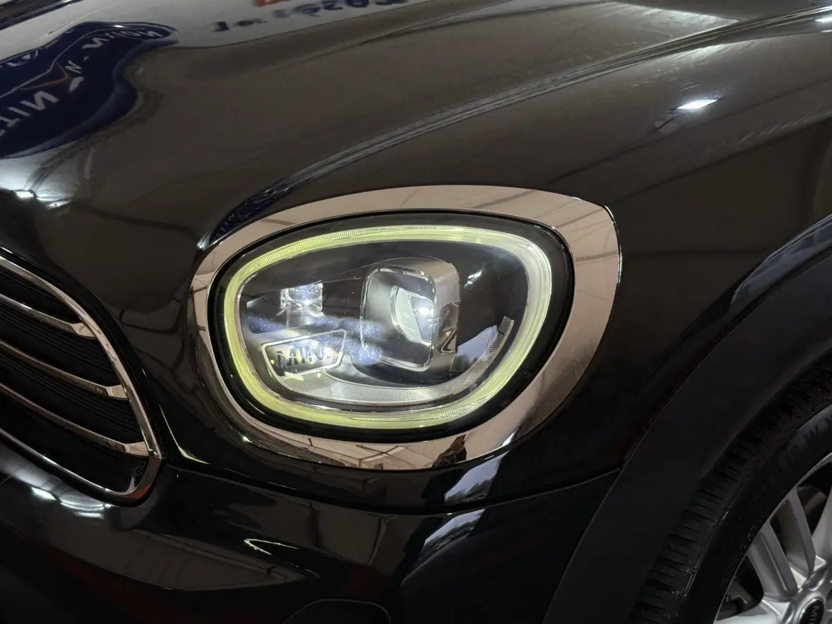 Gros plan sur le phare avant droit LED d'une MINI Countryman noire, soulignant son design moderne et ses finitions chromées.