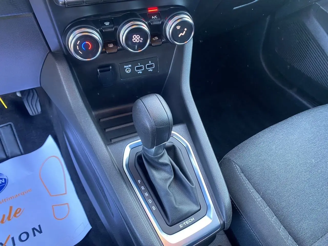 Gros plan sur la console centrale noire de la Renault Clio V E-Tech 140 avec levier de boîte auto et commandes de climatisation.