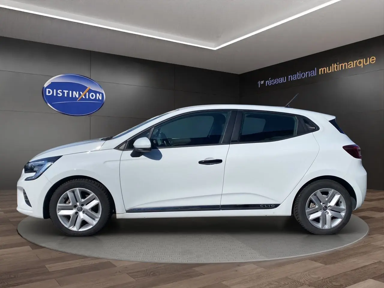 Profil côté gauche d'une Renault Clio V blanche, version E-TECH 140 Business, sur fond intérieur showroom.