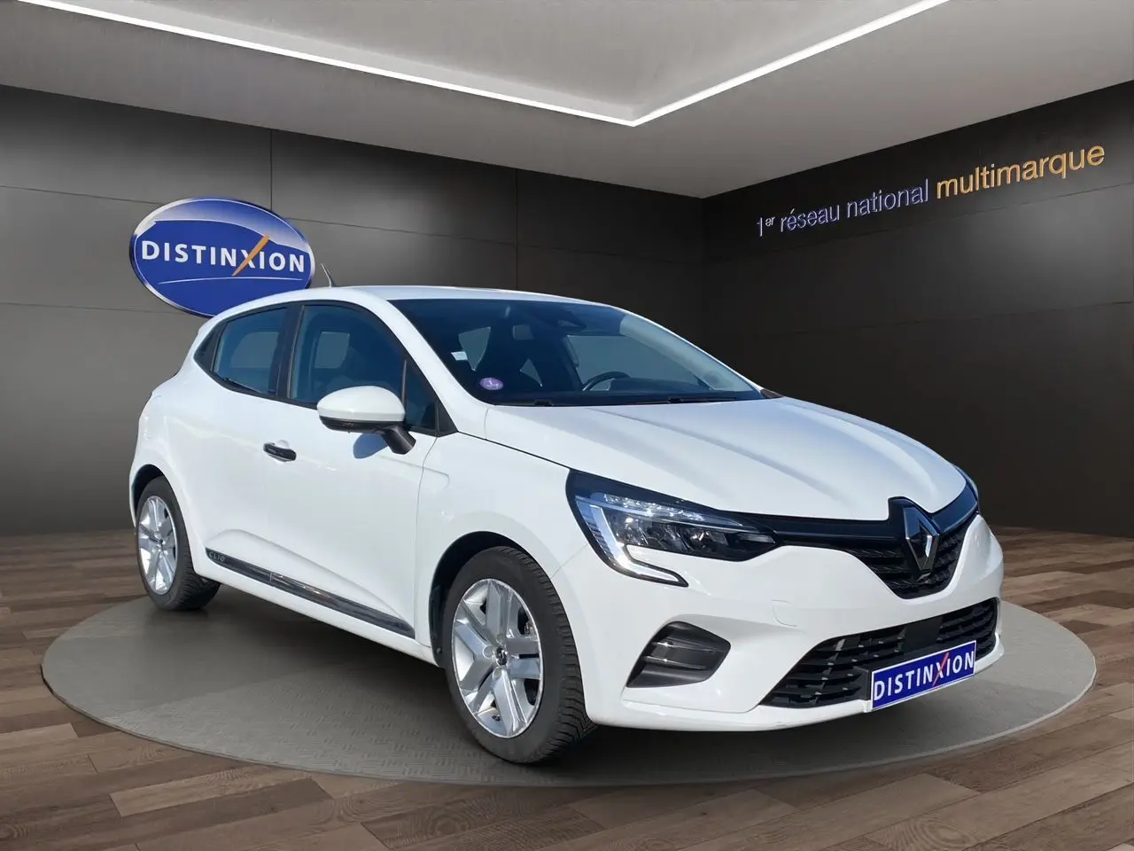 Renault Clio V E-Tech blanc en 3/4 avant droit, avec calandre noire et jantes alliage visibles en showroom.