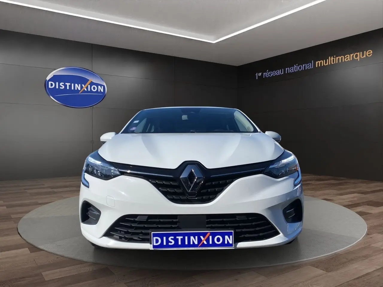 Vue avant d'une Renault Clio V blanche, avec calandre noire et logo Renault centré, en showroom Distinxion.