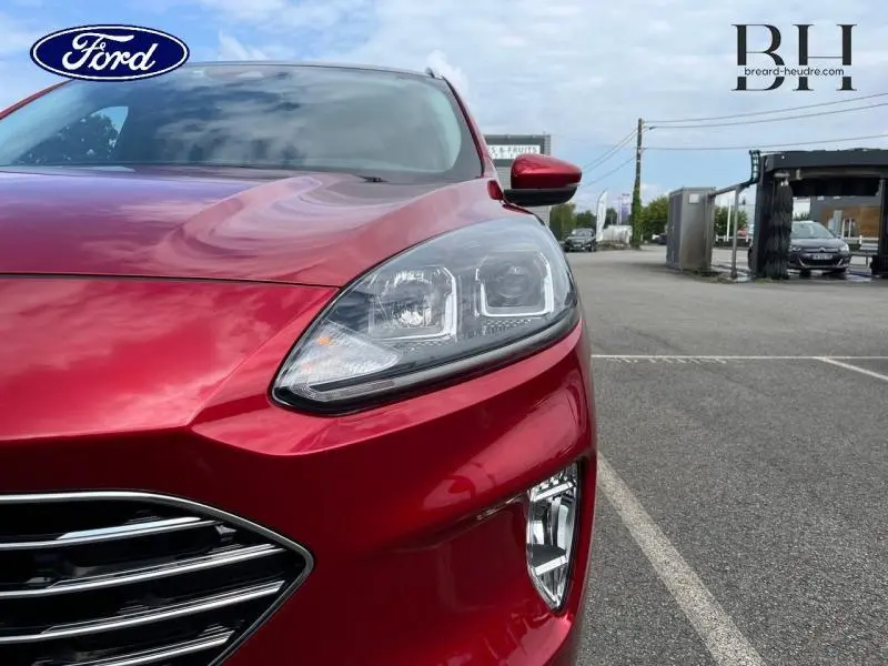 Gros plan sur l'avant droit du Ford Kuga 2022 en rouge Premium Lucid, mettant en valeur son phare LED et la calandre chromée.