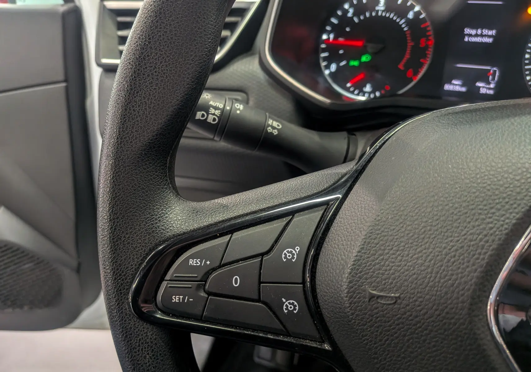 Gros plan sur le volant côté gauche de la Renault Clio V blanche, montrant les commandes de régulateur de vitesse et le tableau de bord flou.