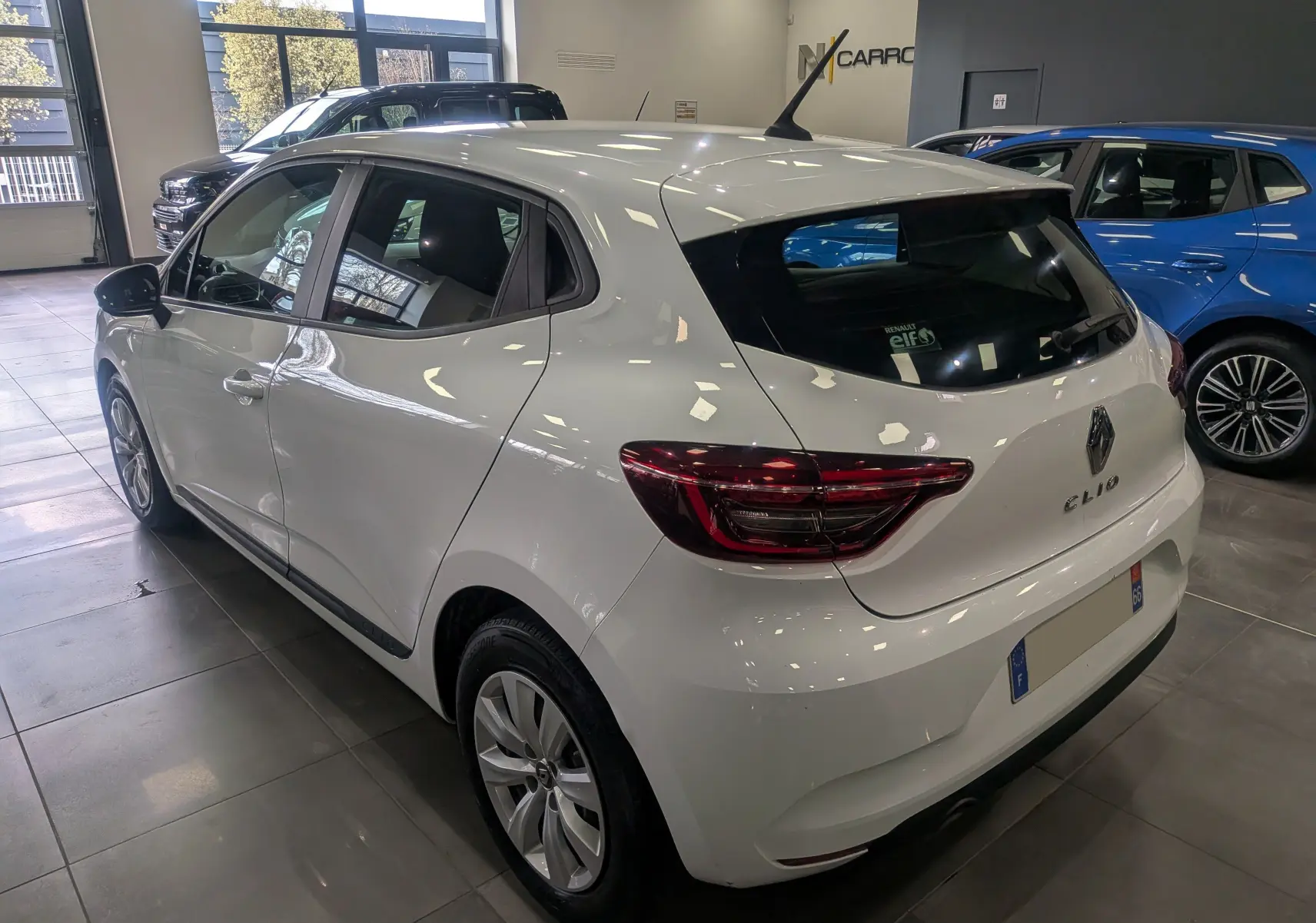 Vue 3/4 arrière droite d'une Renault Clio V blanche Glacier en showroom, avec feux arrière LED et antenne requin.
