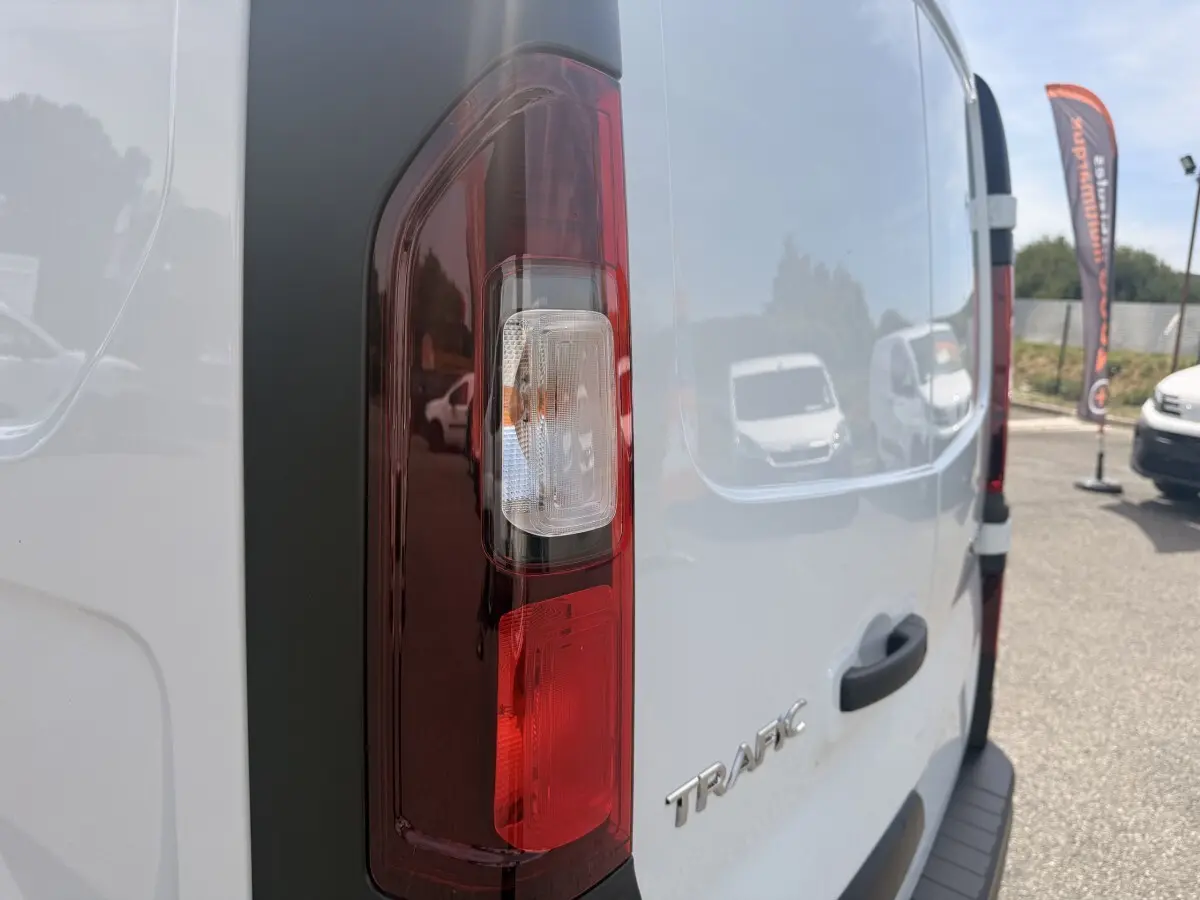 Vue arrière droite du Renault Trafic Fourgon blanc avec feu arrière vertical et logo TRAFIC visible.