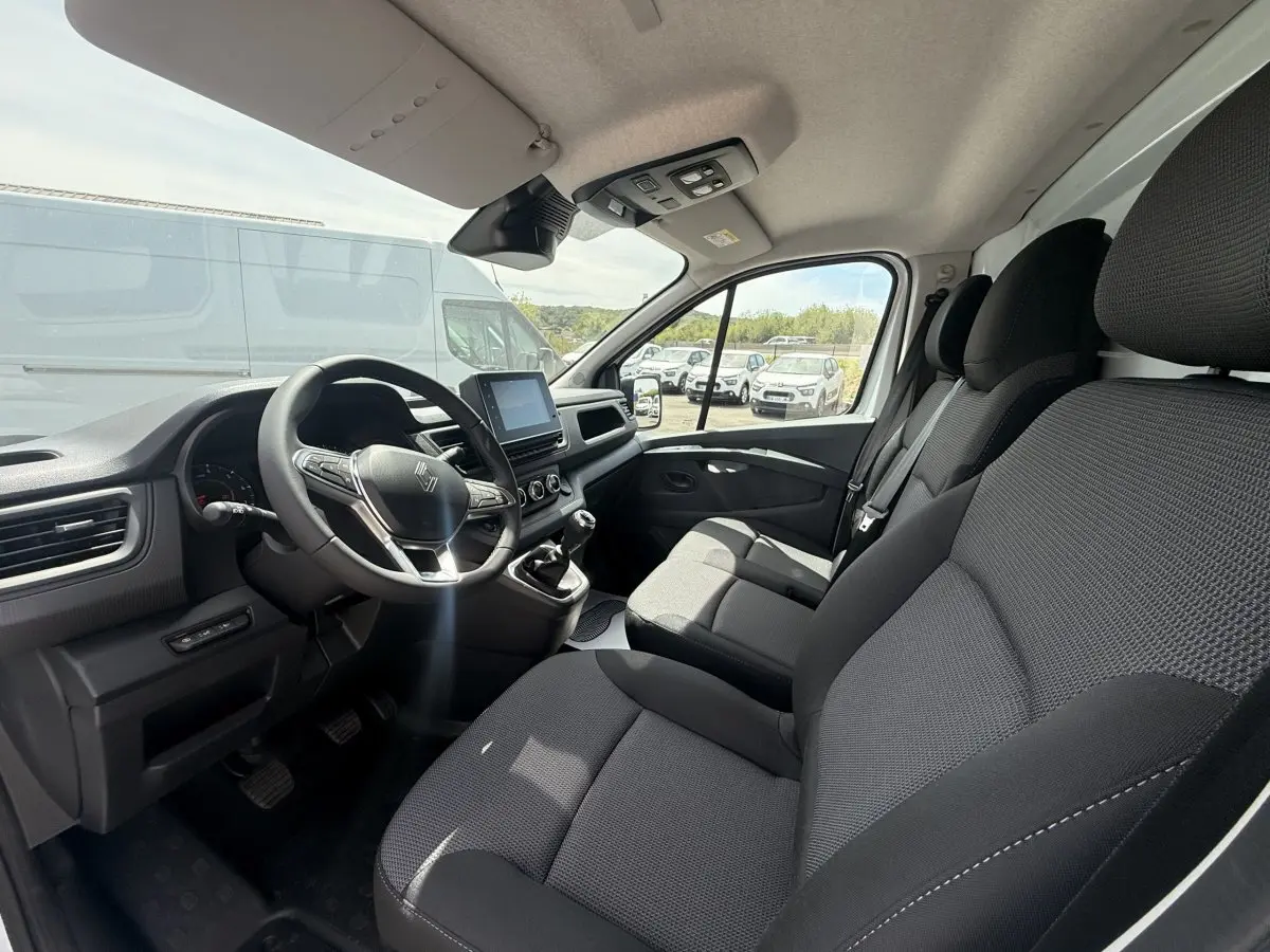 Vue intérieure avant droite du Renault Trafic Fourgon 2025, montrant les sièges noirs et le tableau de bord avec écran tactile.
