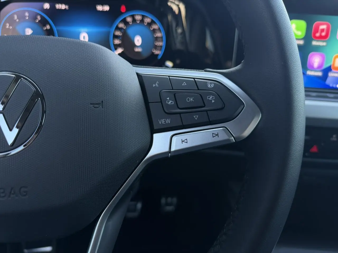 Gros plan sur le volant multifonction noir de la Volkswagen Golf 8 avec commandes intégrées et tableau de bord numérique en arrière-plan.