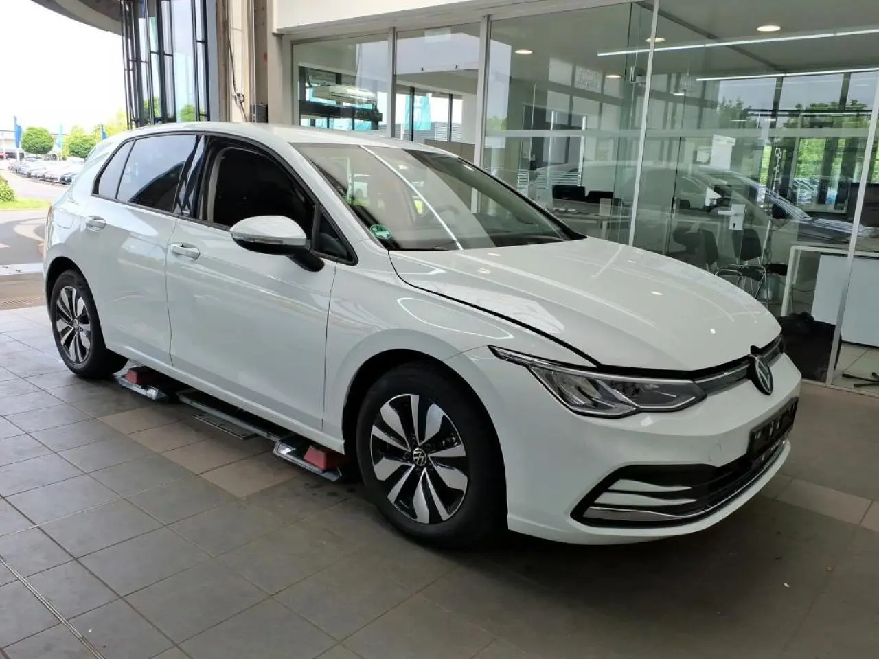 Volkswagen Golf 8 blanche vue 3/4 avant droit en intérieur, avec jantes alliage et feux LED distinctifs.