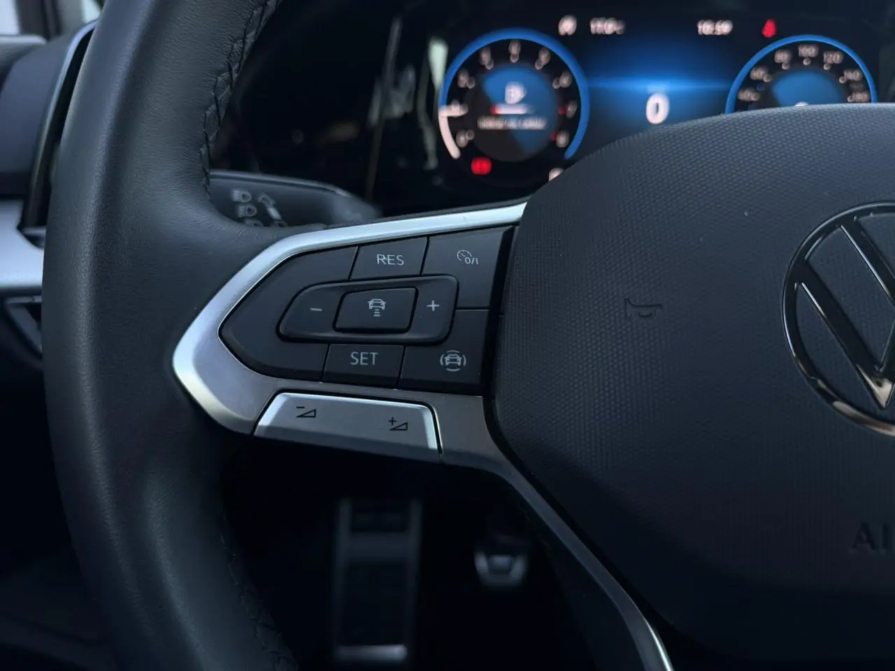 Gros plan sur le volant multifonction noir de la Volkswagen Golf 8 avec commandes intégrées et tableau de bord numérique en arrière-plan.
