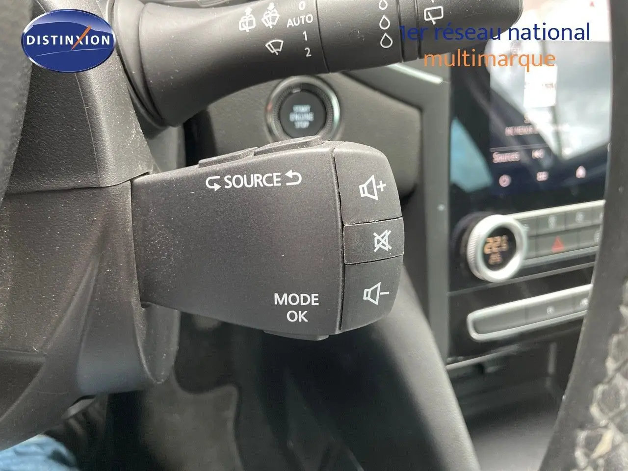 Gros plan sur la commande au volant de la Renault Mégane Break 1.6E-TECH 2021, avec tableau de bord et écran tactile en arrière-plan.