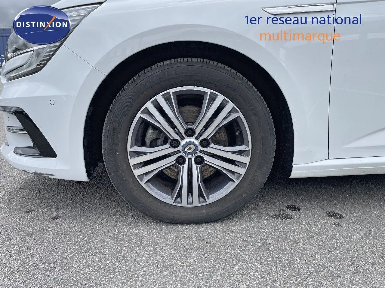 Gros plan sur la roue avant droite d’une Renault Mégane Break blanc glacier avec jante alliage distinctive.