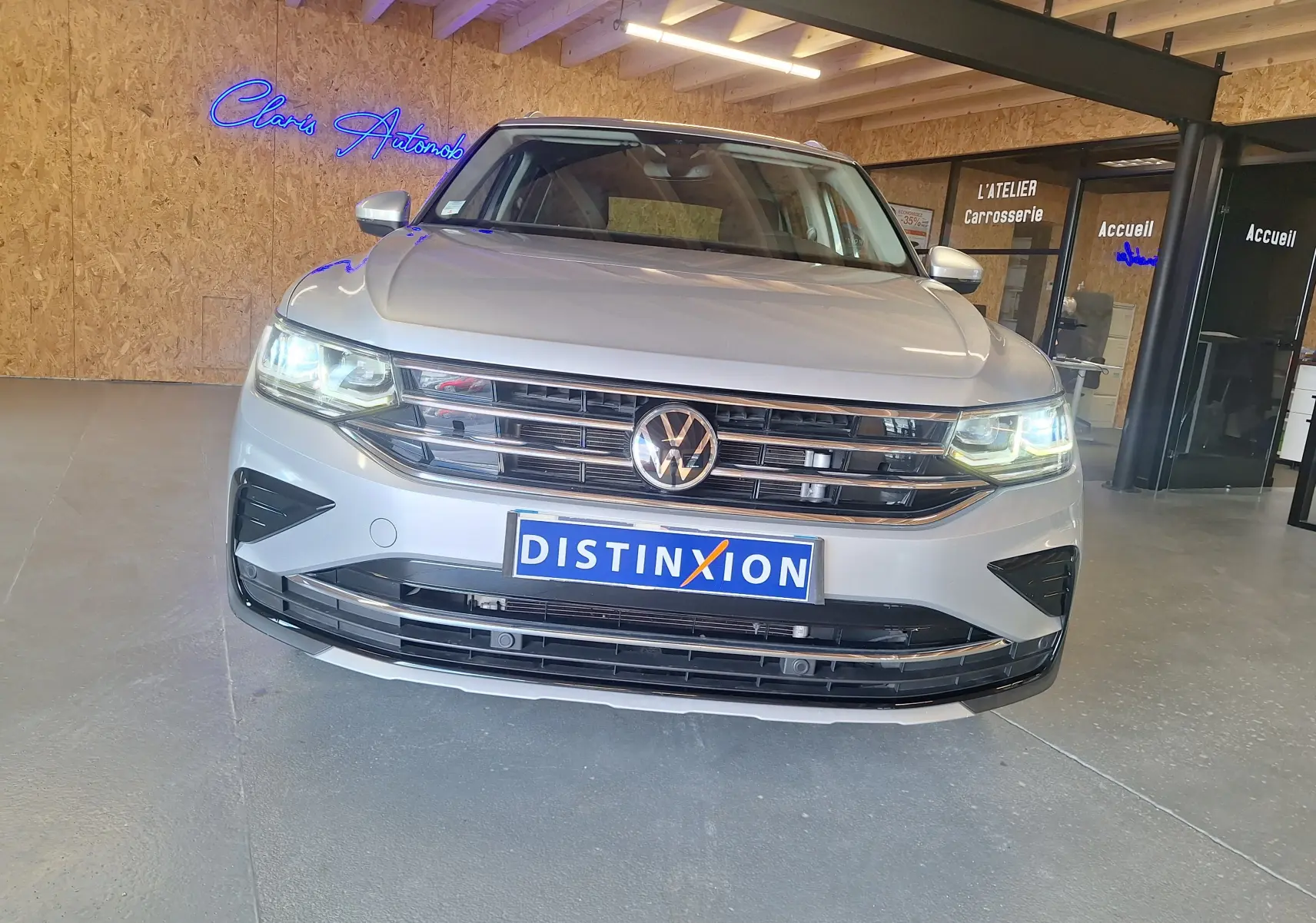 Vue frontale d'un Volkswagen Tiguan gris métallisé, avec phares allumés et calandre chromée dans un showroom.