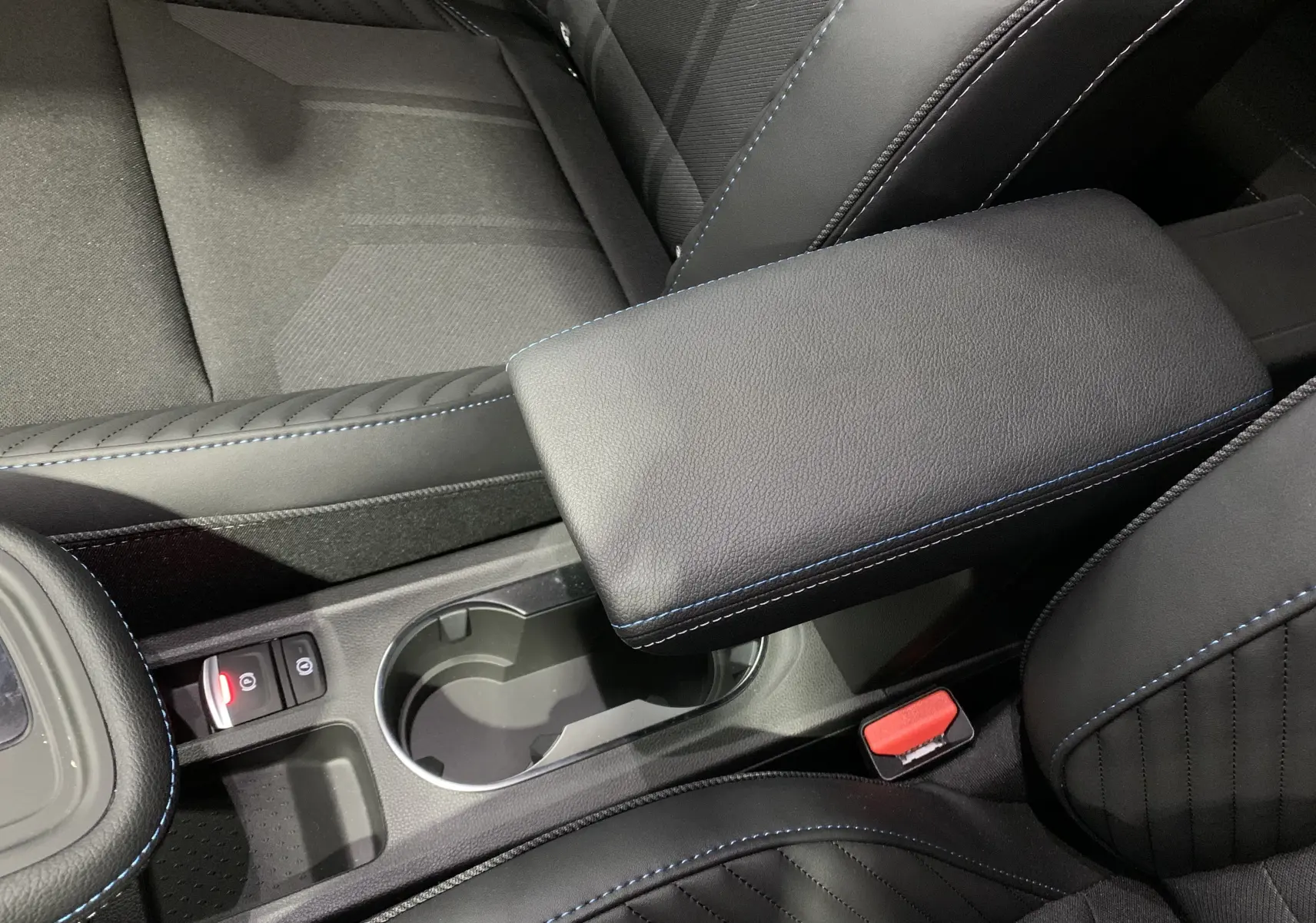 Gros plan sur l'accoudoir central noir avec surpiqûres bleues et porte-gobelets dans l'habitacle du Renault Symbioz.