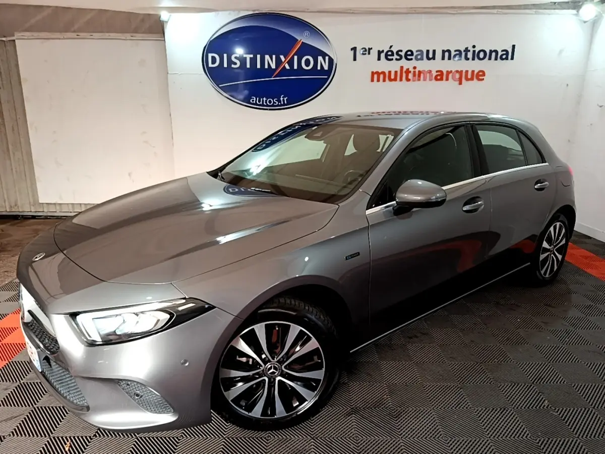 Vue 3/4 avant droit d'une Mercedes Classe A 250 e Business Line gris foncé avec phares LED allumés en intérieur showroom