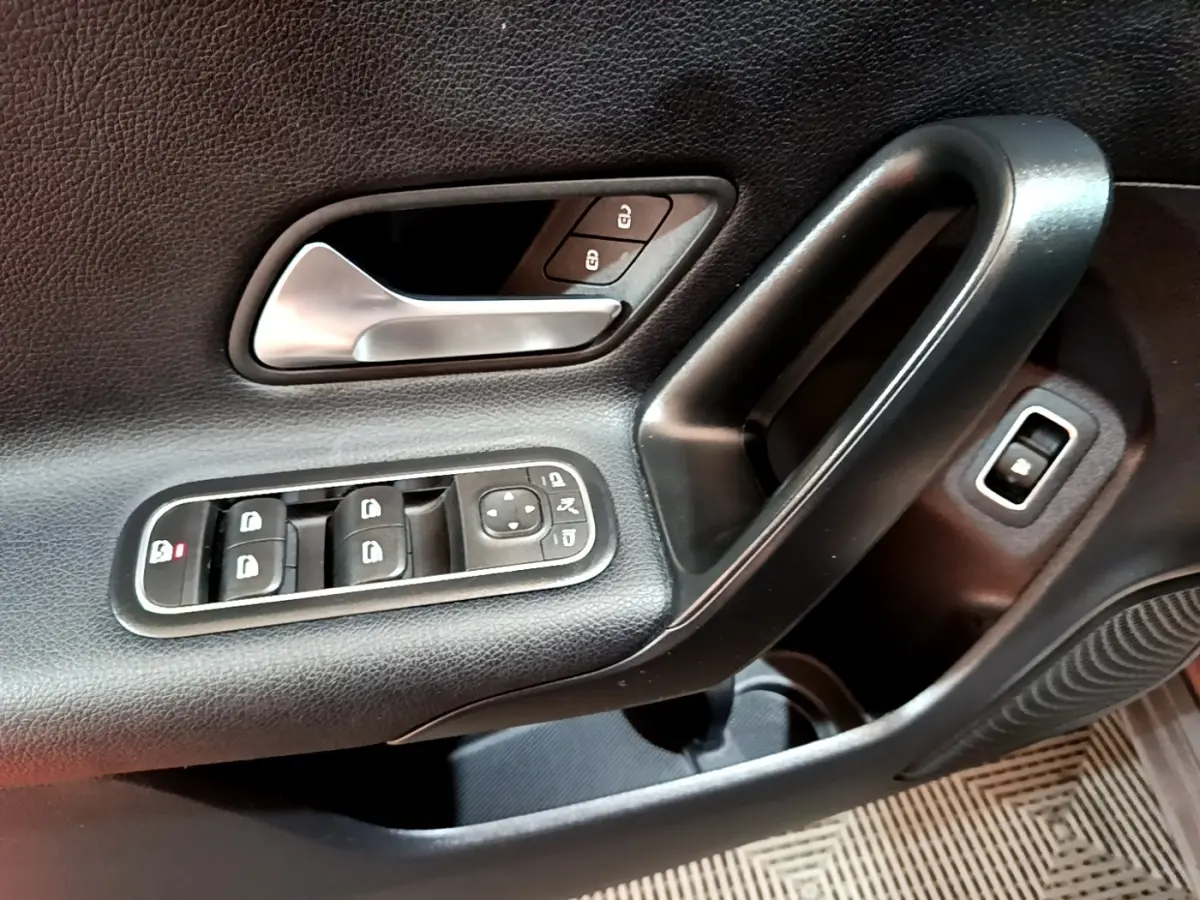 Gros plan sur la poignée intérieure et les commandes de porte côté gauche d'une Mercedes Classe A gris foncé.