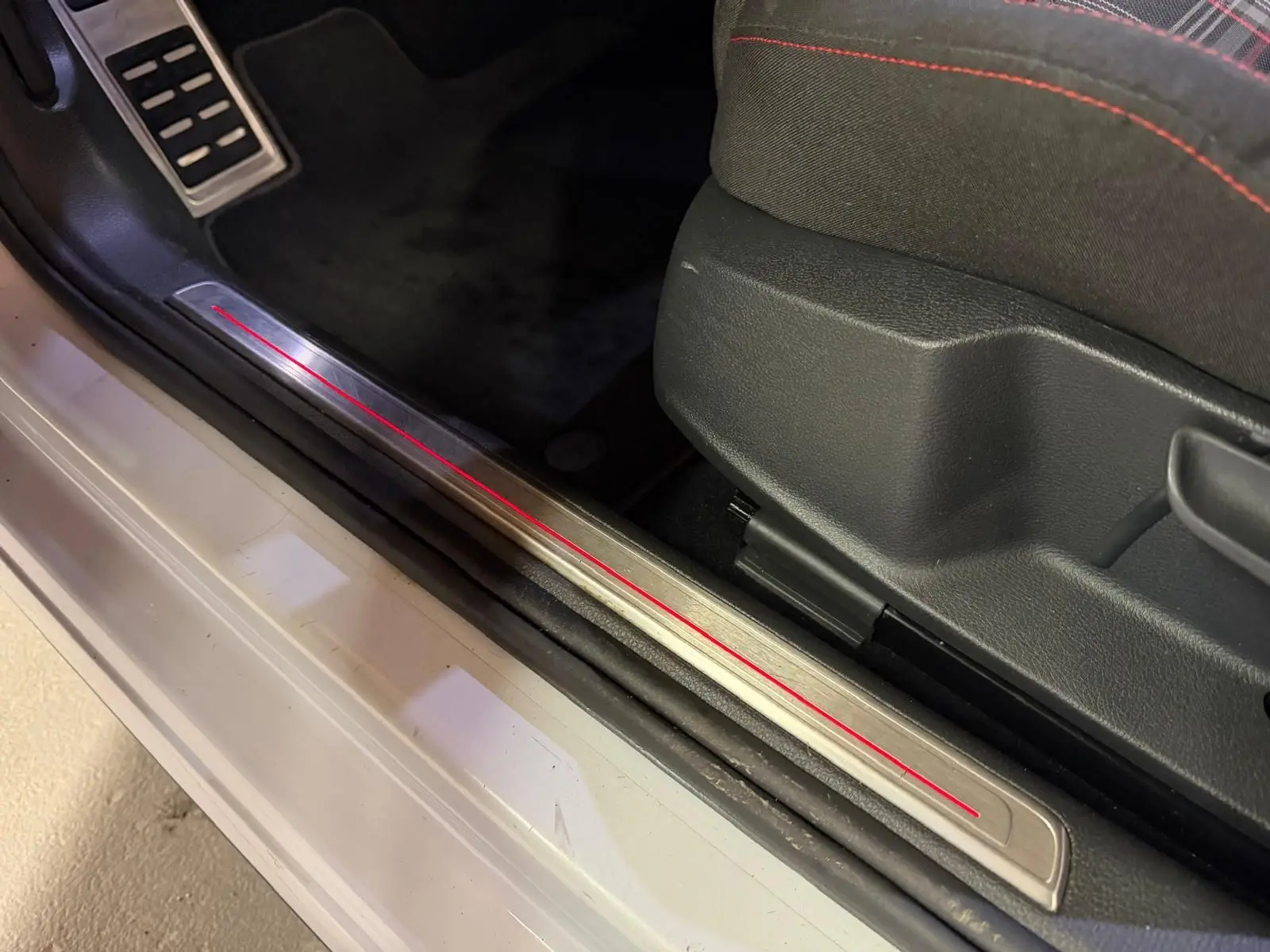 Gros plan sur la partie basse intérieure côté conducteur d'une Volkswagen Golf GTI Performance gris, avec seuil de porte en métal.