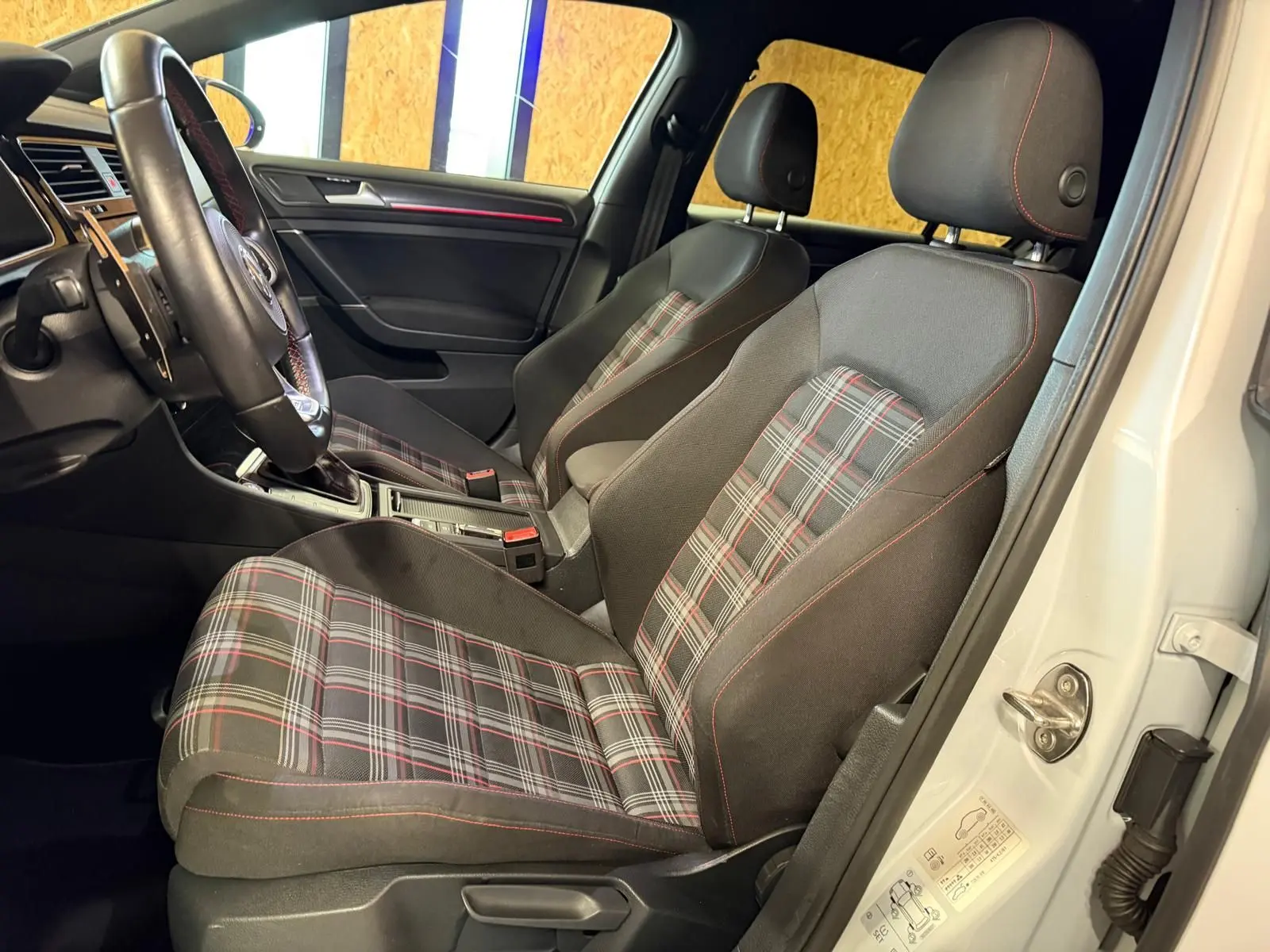 Gros plan sur le volant noir avec surpiqûres rouges et tableau de bord numérique de la Volkswagen Golf GTI Performance gris.