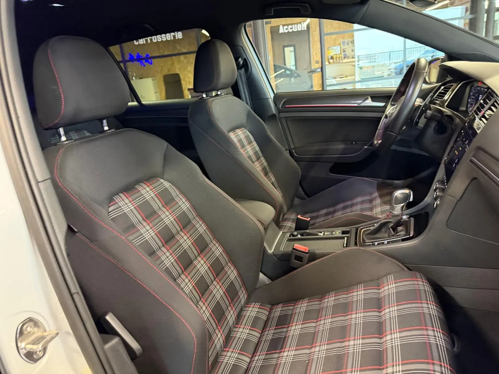 Vue intérieure côté conducteur d’une Volkswagen Golf GTI Performance 2018 avec sièges sport à motif tartan et coutures rouges.