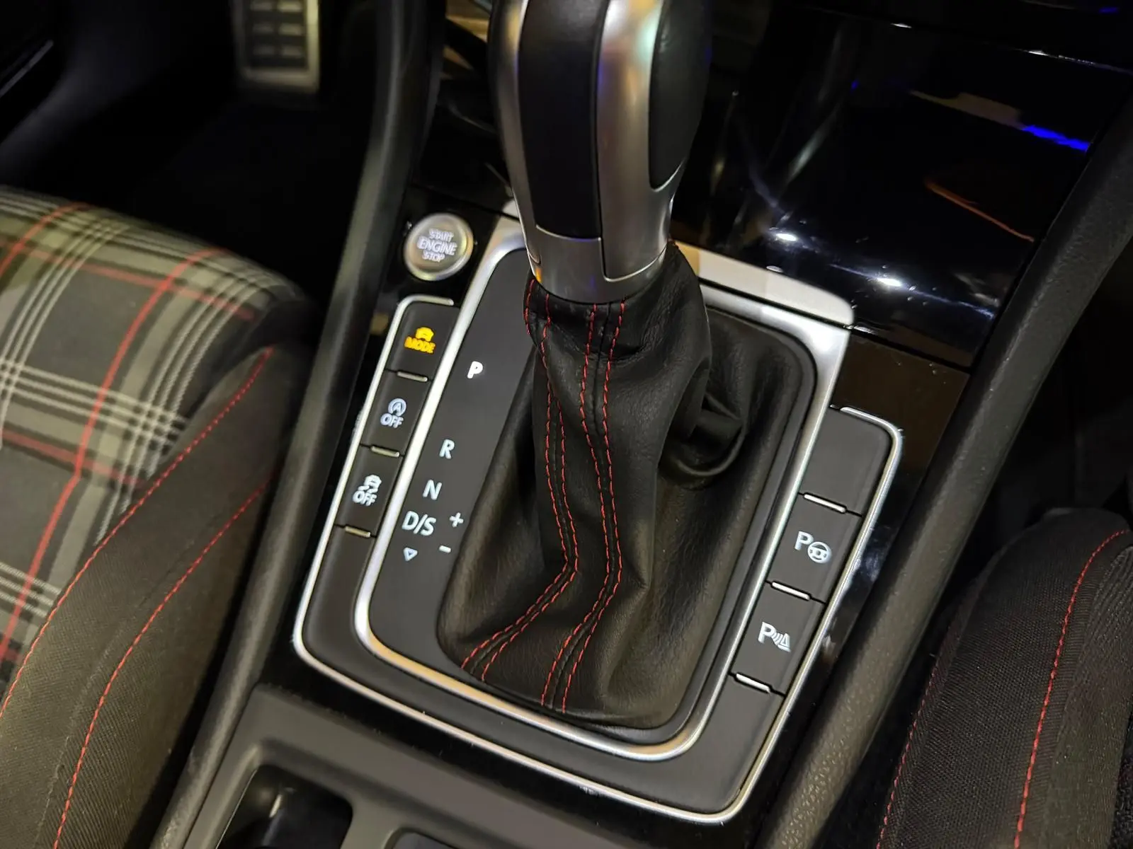 Gros plan sur la console centrale de la Volkswagen Golf GTI gris, avec levier de vitesse automatique et coutures rouges.