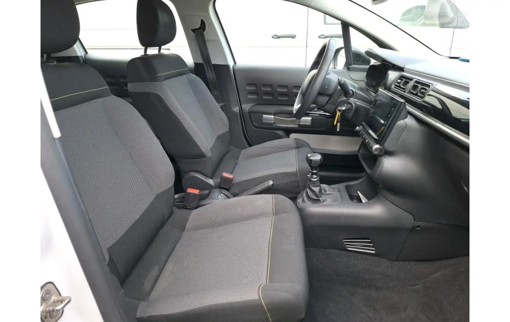 Intérieur avant de la Citroën C3 blanc, vue côté gauche, sièges gris avec surpiqûres jaunes et tableau de bord moderne.