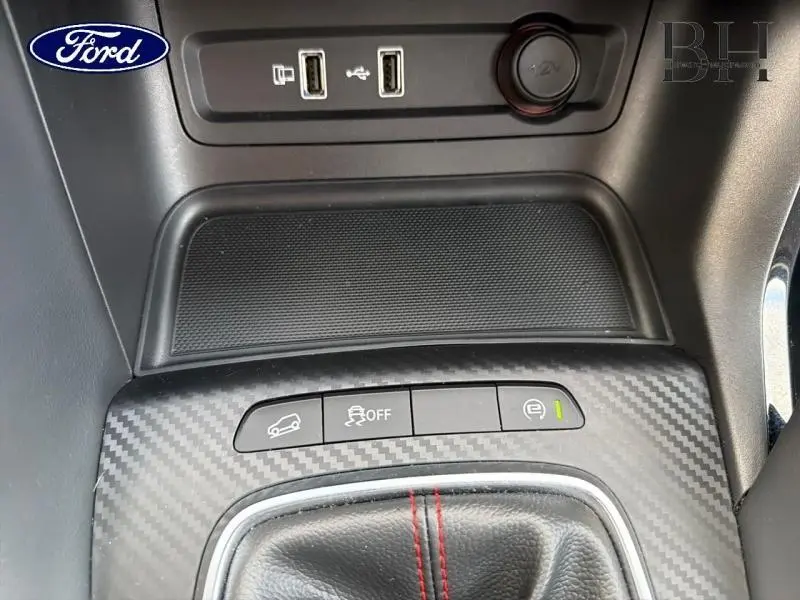 Gros plan sur la console centrale avec finition carbone et boutons de contrôle, prise 12V et ports USB visibles.