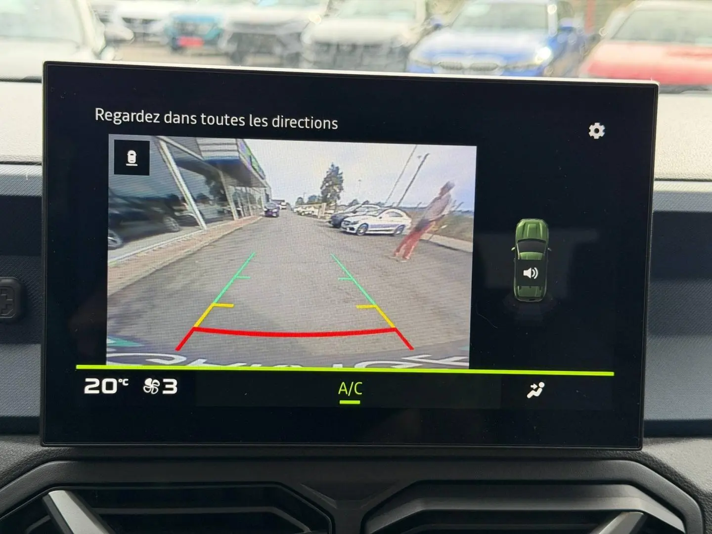 Écran tactile intérieur montrant la caméra de recul avec vue arrière sur une route et un piéton flou.