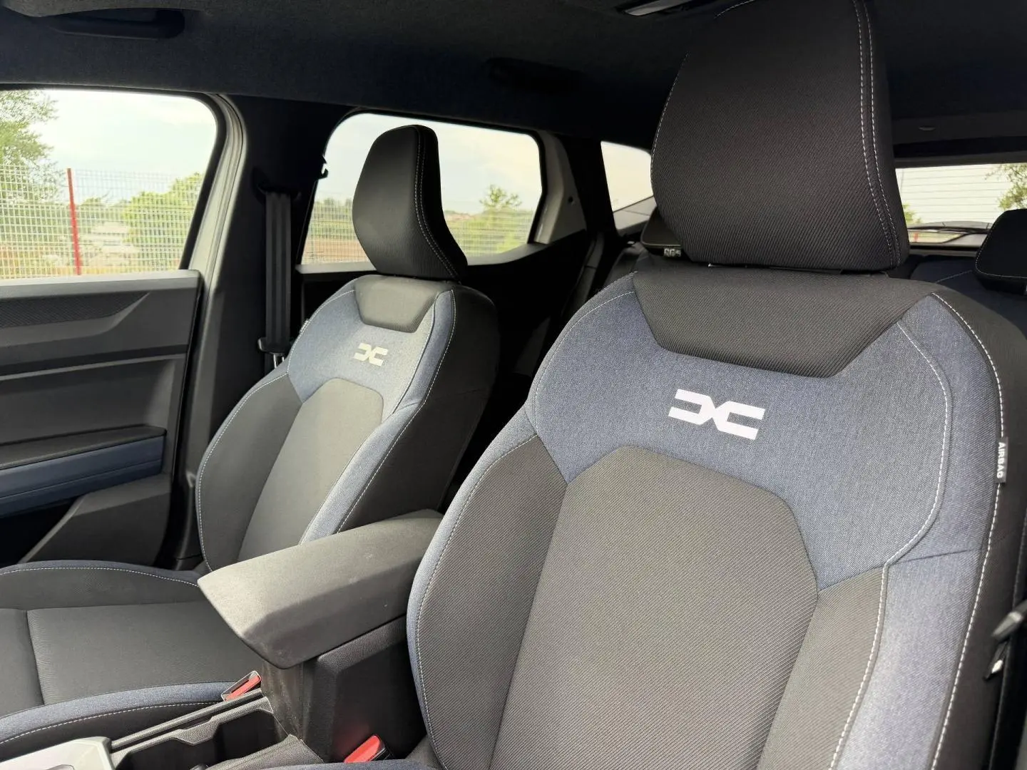 Gros plan sur les sièges avant du Dacia Duster 2025 version Journey, tissu Denim avec logo réfléchissant et accoudoir central.