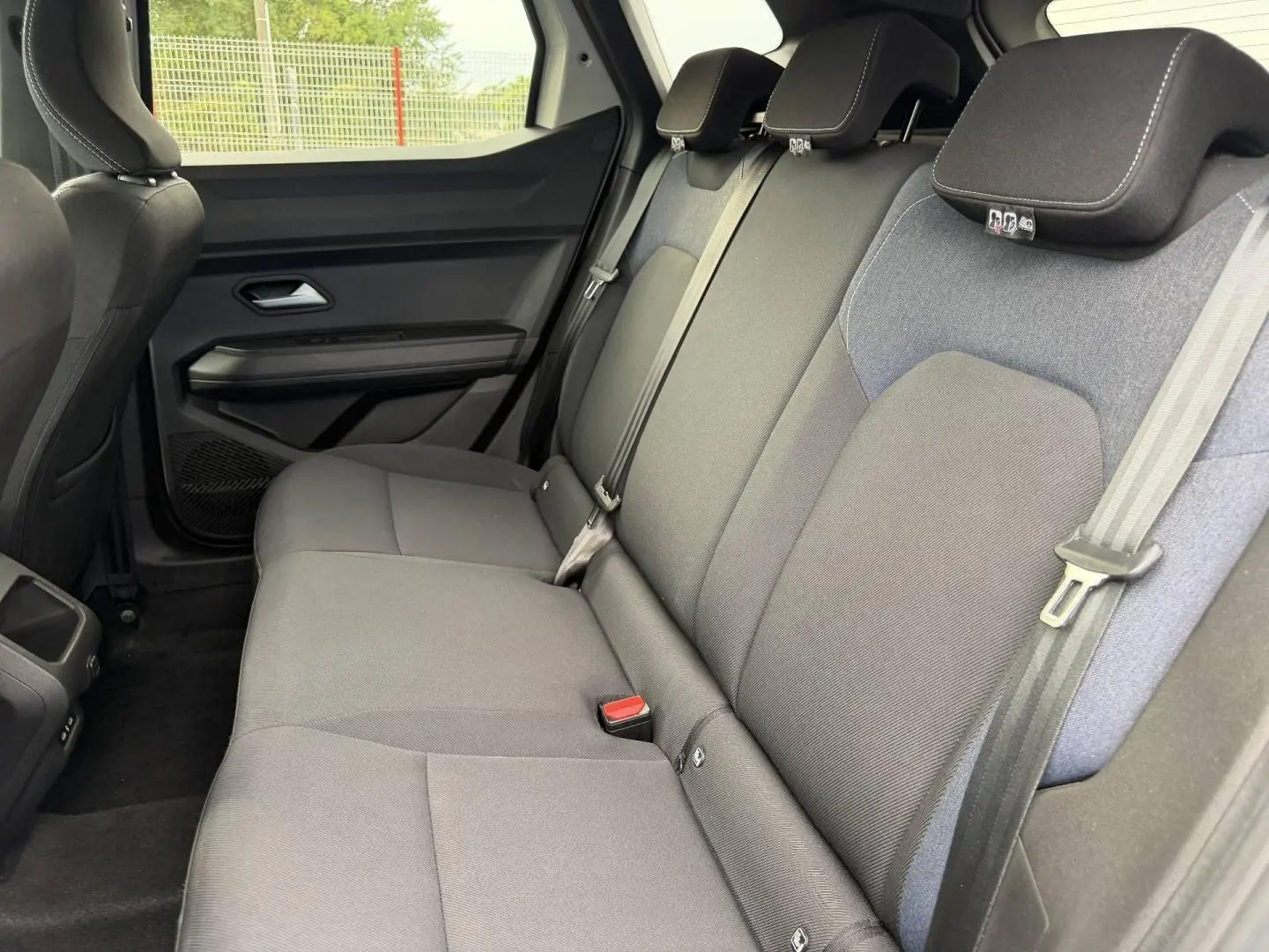 Vue latérale intérieure des sièges arrière gris foncé du Dacia Duster 2025, avec appuie-têtes et ceintures de sécurité visibles.