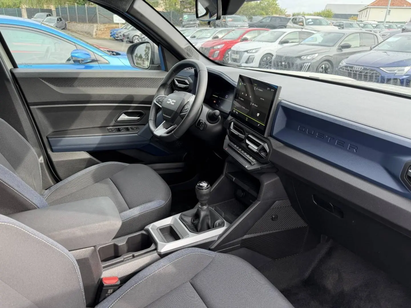 Intérieur du Dacia Duster 2025 vue côté conducteur, planche de bord bleu Sandstone avec écran tactile et boîte manuelle.