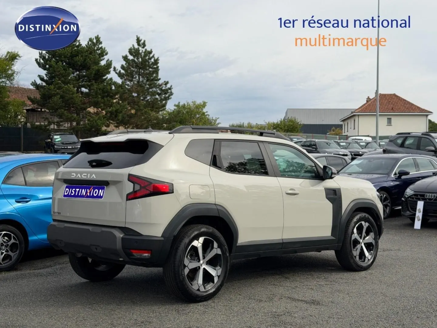 Vue 3/4 arrière droite d'un Dacia Duster 2025 Sandstone avec jantes alu et barres de toit visibles en extérieur.