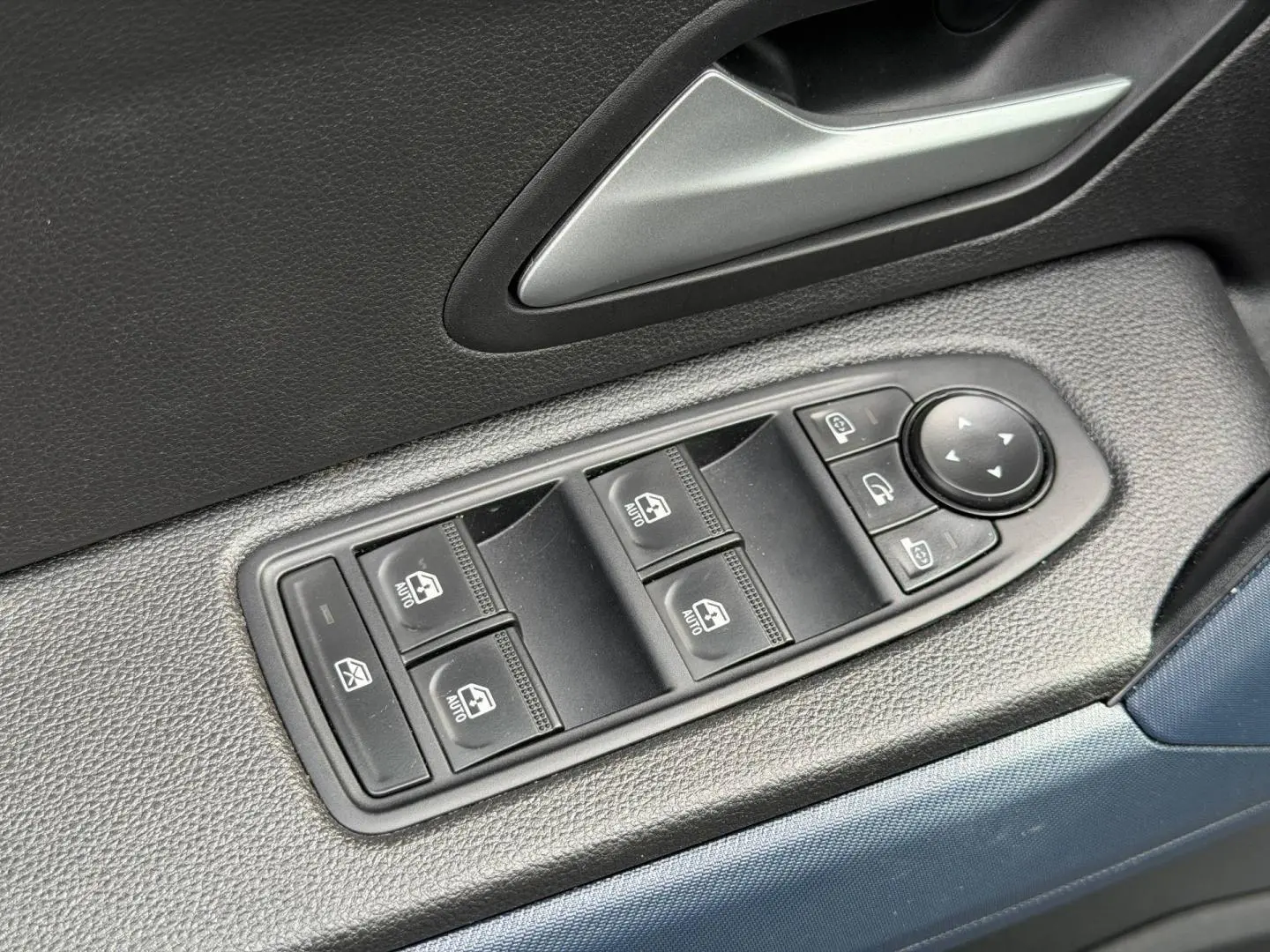 Gros plan sur les commandes des vitres électriques côté conducteur du Dacia Duster 2025 finition Journey couleur Sandstone.