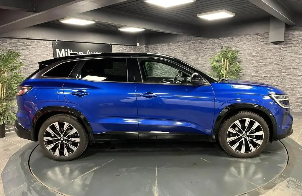 Profil côté gauche du Renault Austral 2023 bleu avec toit noir et jantes alliage noires diamantées dans un showroom.
