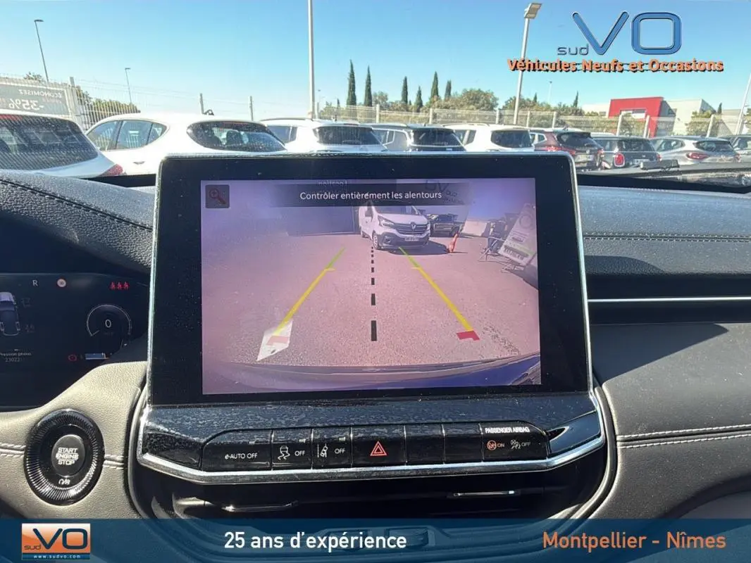 Vue intérieure du tableau de bord du Jeep Compass gris 2023 avec écran tactile affichant la caméra de recul et commandes centrales visibles.
