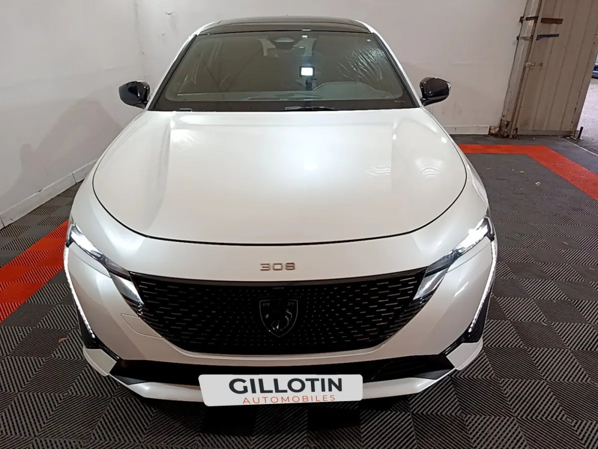 Vue frontale d'une Peugeot 308 PHEV 180 E-EAT8 GT blanche avec calandre noire et phares LED allumés.