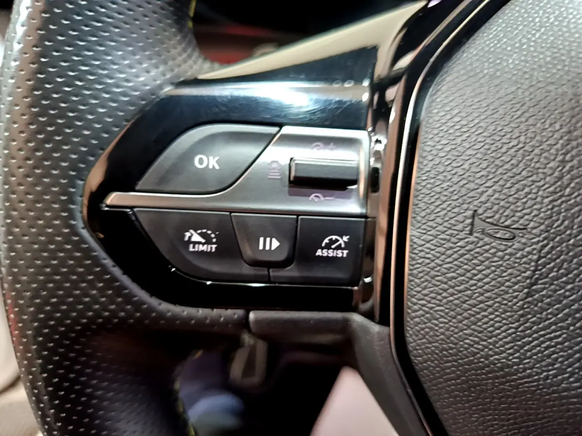 Gros plan sur les commandes gauche du volant cuir perforé du Peugeot 308 PHEV 180 E-EAT8 GT blanc de 2022.