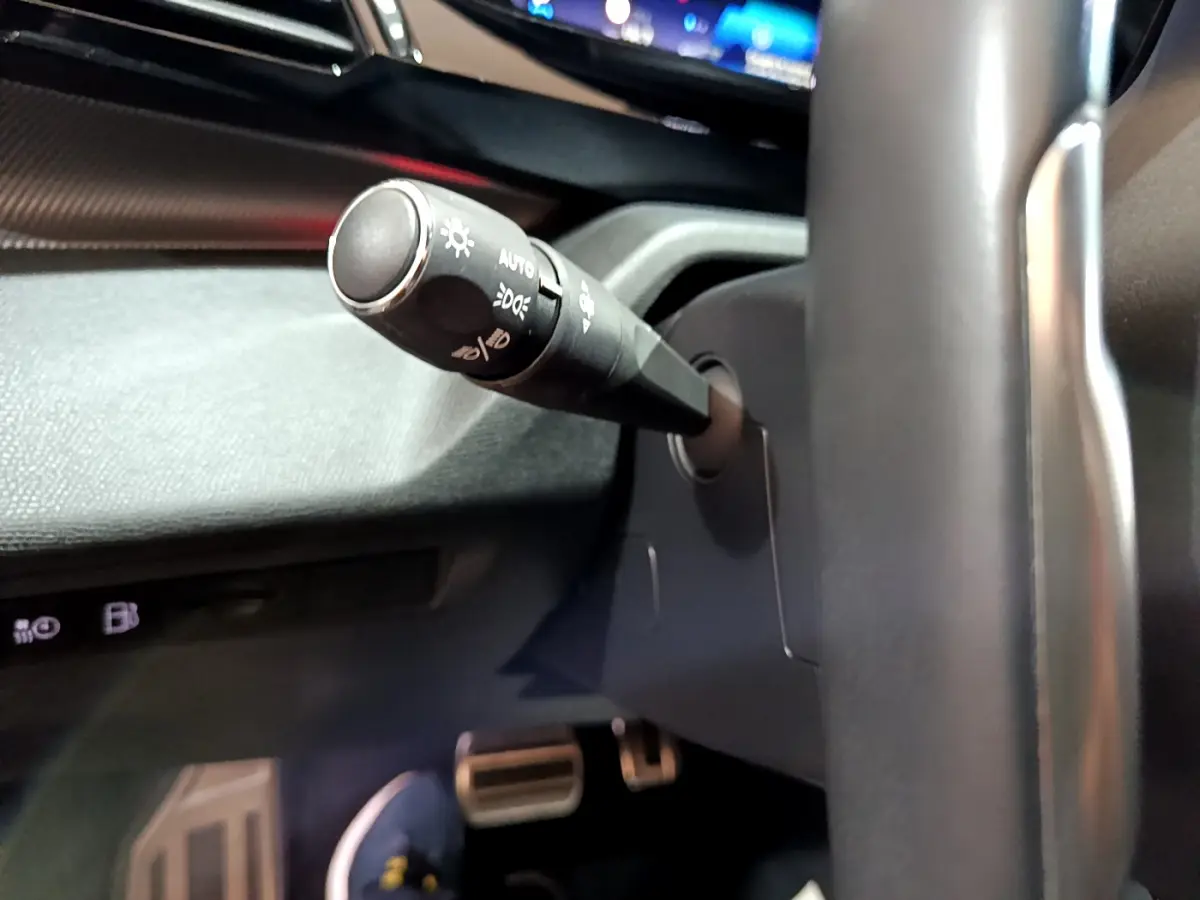 Gros plan sur la manette de commande d'éclairage à gauche du volant dans l'habitacle sombre d'une Peugeot 308 PHEV blanche.