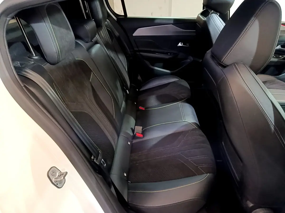 Vue côté gauche de l'habitacle arrière de la Peugeot 308 PHEV 180 E-EAT8 GT 2022 avec sièges noirs et surpiqûres vertes.