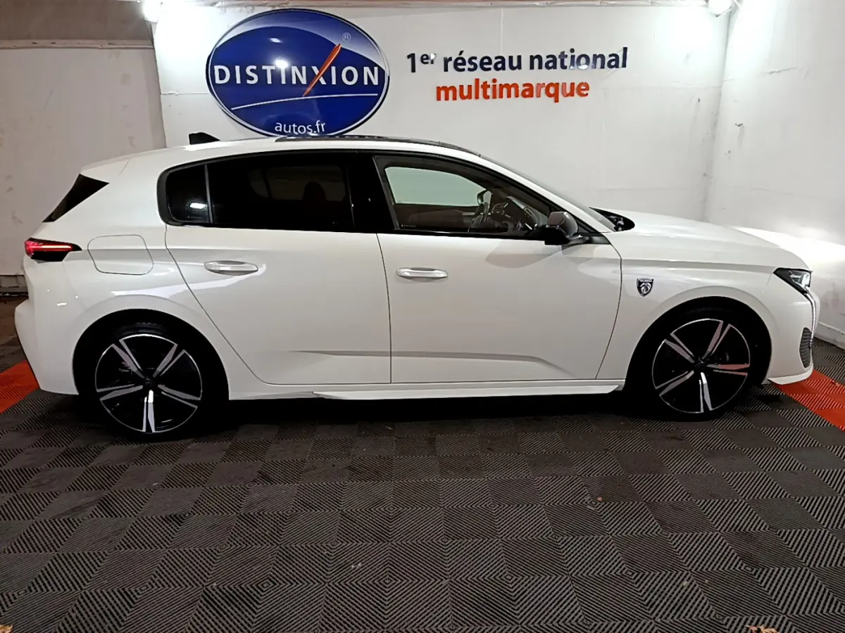 Peugeot 308 PHEV 180 E-EAT8 GT blanc vue de profil côté gauche en intérieur showroom avec jantes noires distinctives