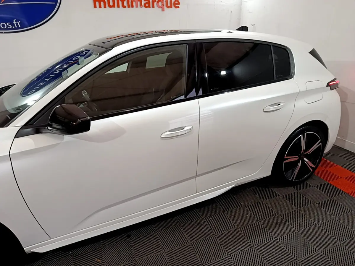 Profil côté gauche d'une Peugeot 308 PHEV 180 E-EAT8 GT blanche, avec vitres teintées et jantes noires stylisées.