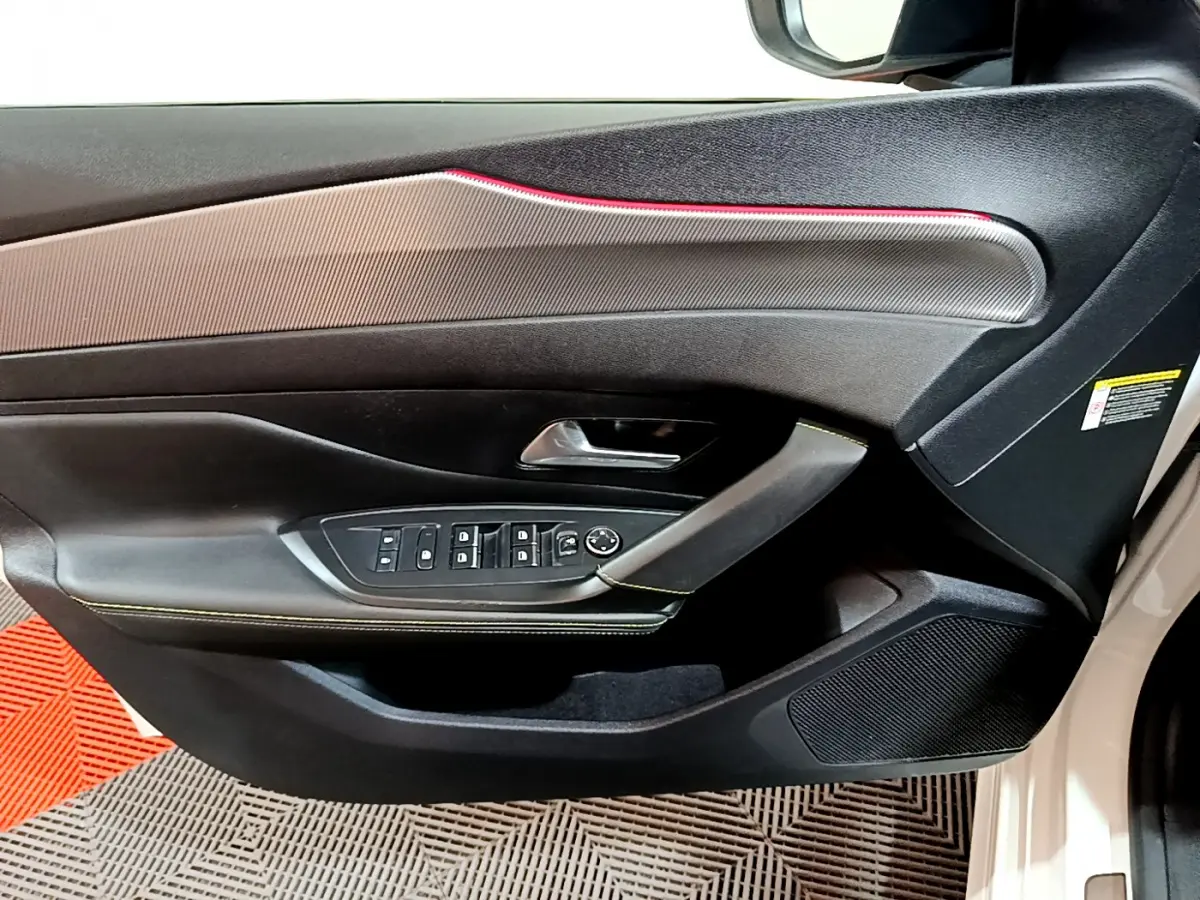 Gros plan sur la porte côté gauche d'une Peugeot 308 PHEV blanche, avec commandes électriques et surpiqûres vertes.